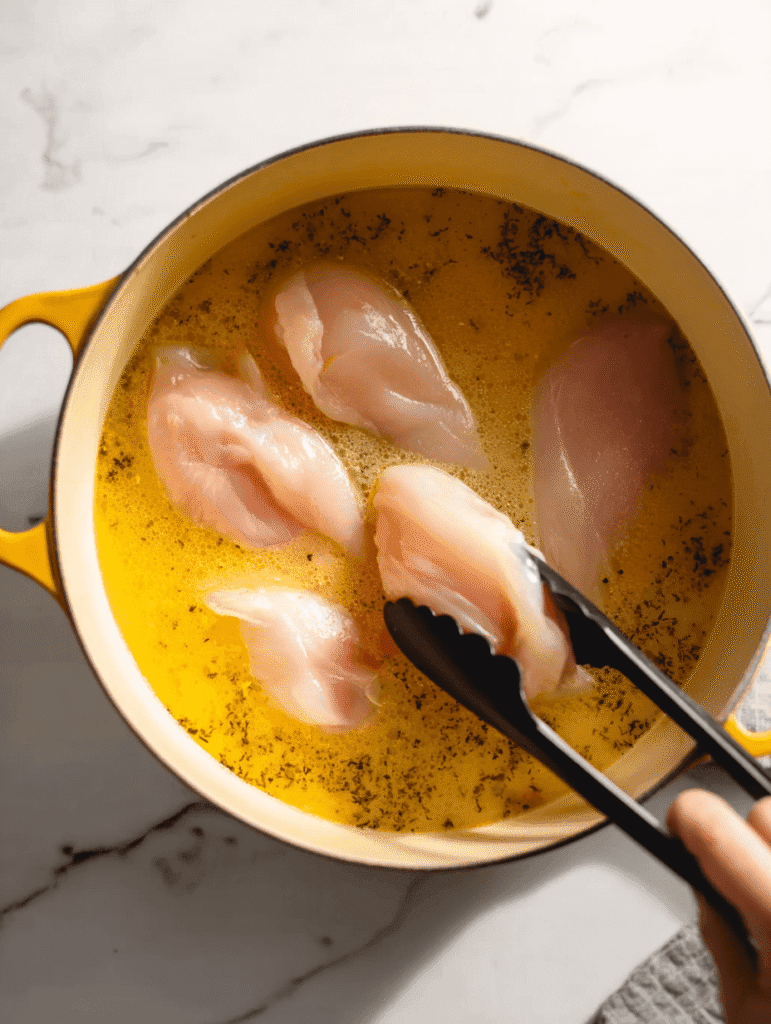 Adding chicken breasts to seasoned broth for lemon chicken orzo soup