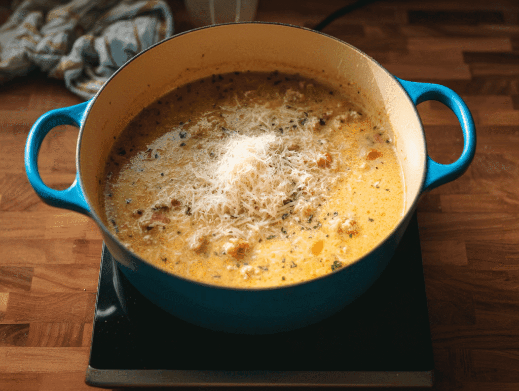Adding grated Parmesan cheese to creamy ground turkey soup in a pot.