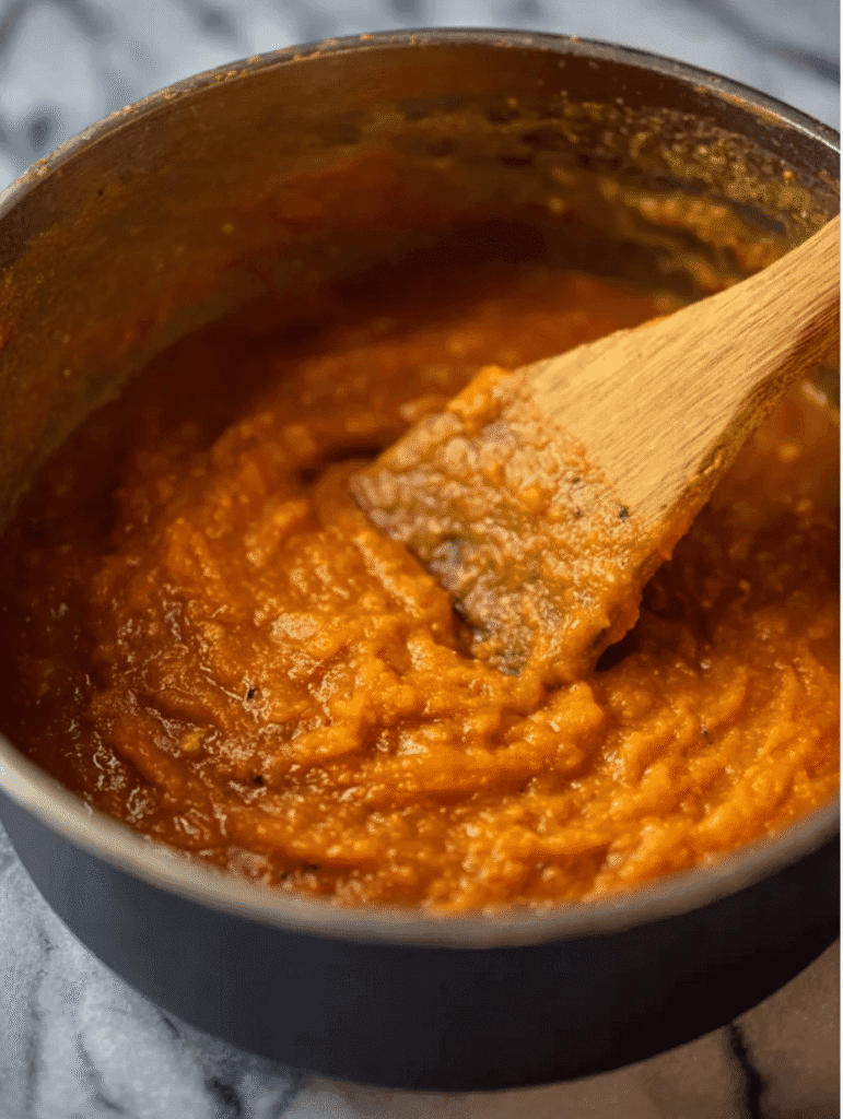 Blended tomato basil soup base in a pot stirred with a wooden spoon