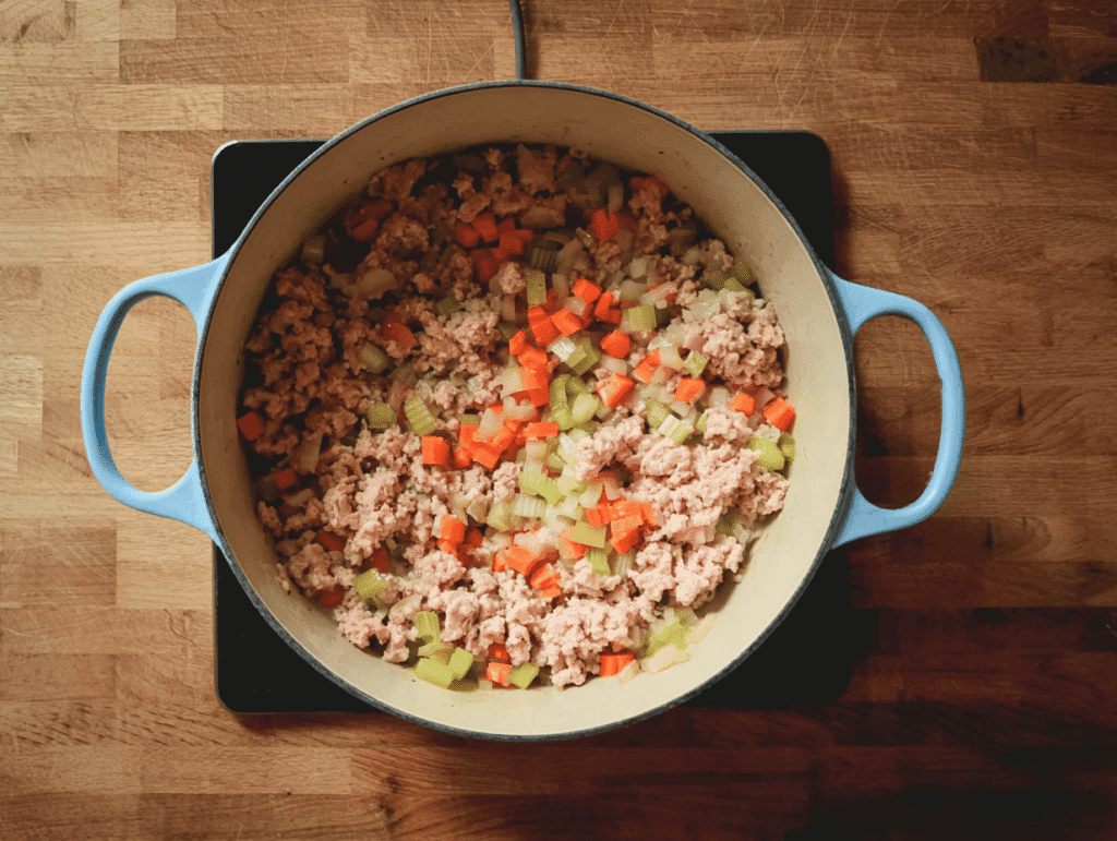 Ground turkey cooking in a pot with onions, carrots, and celery for soup.