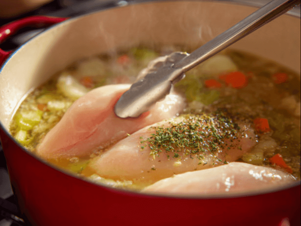 adding raw chicken to simmering broth with vegetables for chicken and wild rice soup recipe