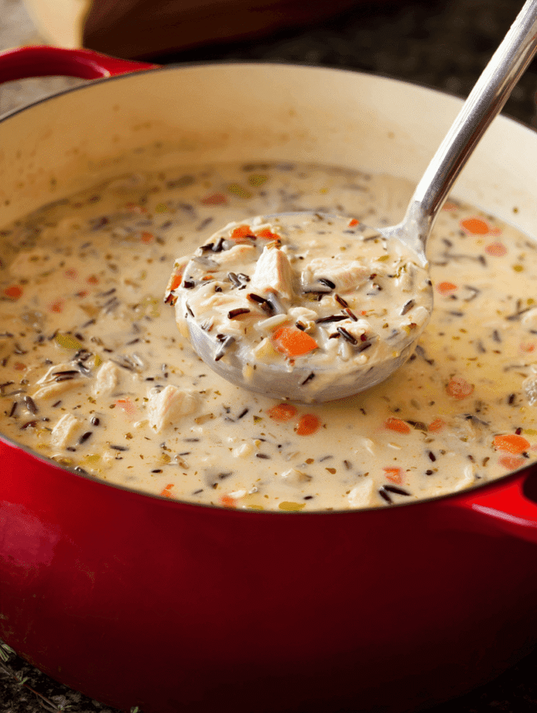 creamy chicken and wild rice soup cooking in red Dutch oven with ladle