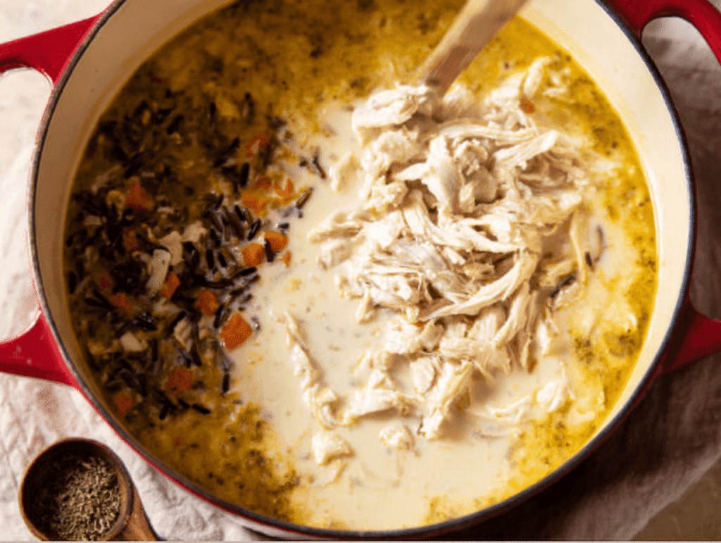 adding shredded chicken, cooked wild rice, and cream to soup pot for chicken and wild rice soup recipe