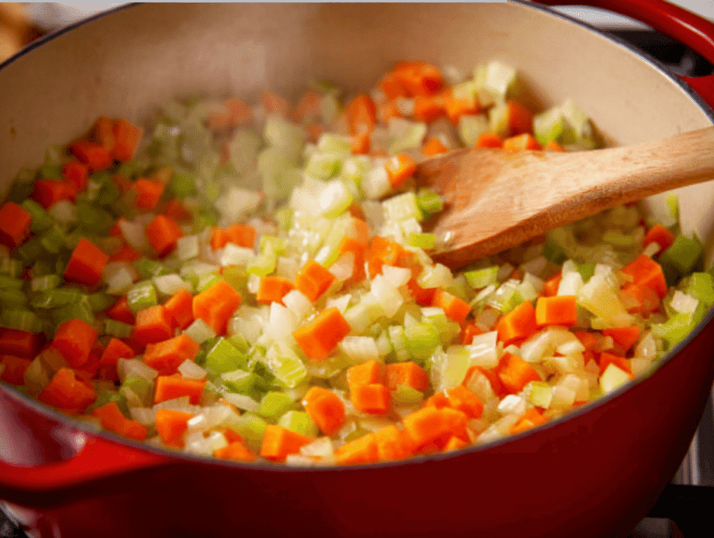 onions carrots and celery sautéing in red pot for chicken and wild rice soup recipe
