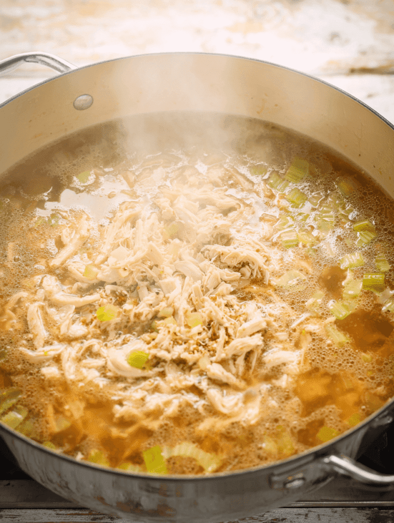 High Protein Chicken Noodle Soup – The Ultimate Cozy 30-Minute Meal 7 Adding shredded chicken to simmering broth for High Protein Chicken Noodle Soup.