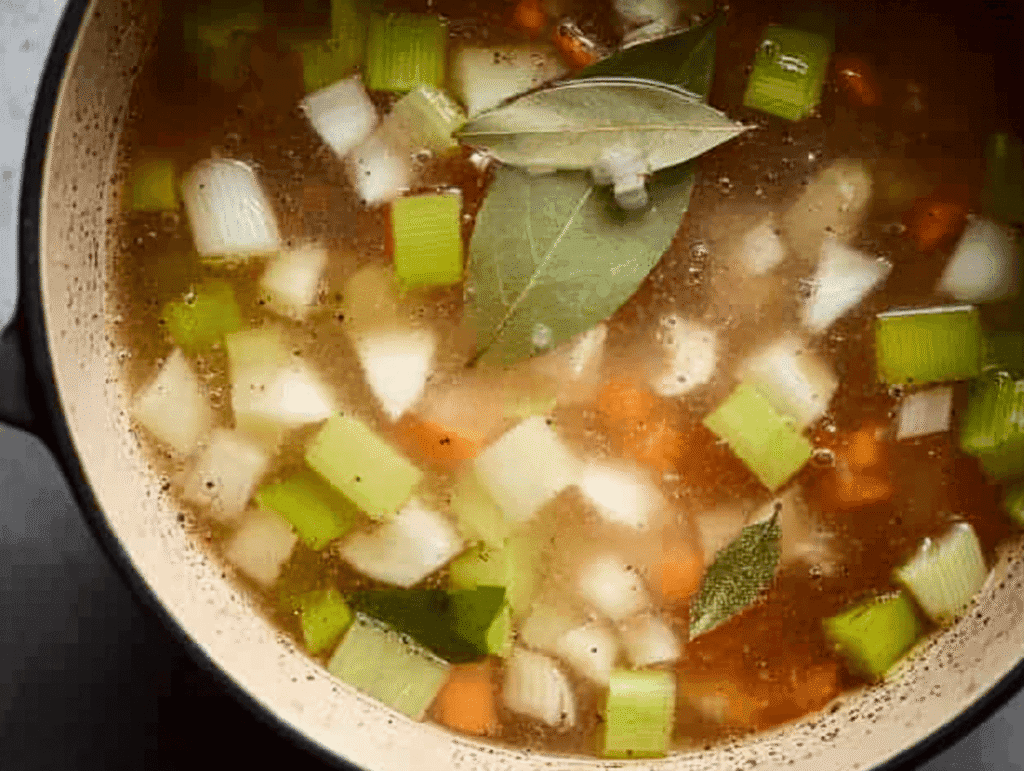 Onions, celery, and carrots simmering in chicken broth with bay leaf for Italian Penicillin Soup Recipe