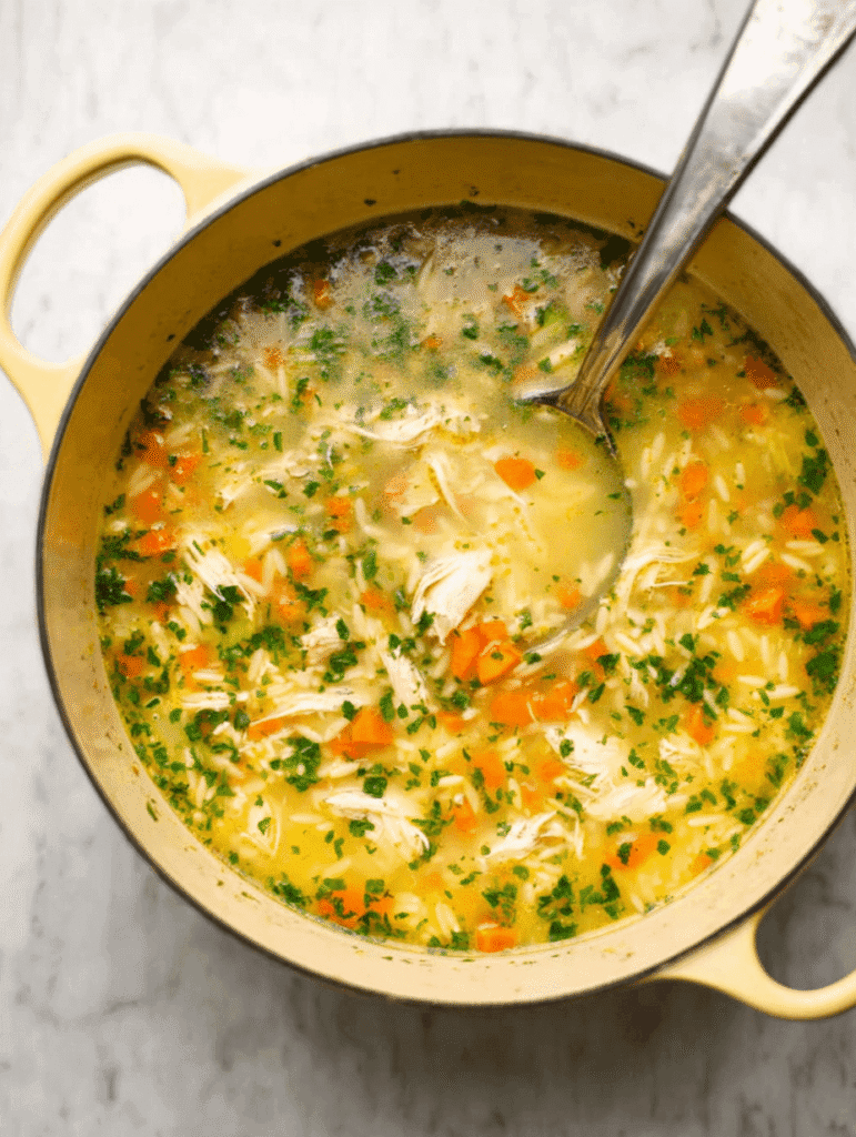 Lemon chicken orzo soup in a yellow pot with a ladle, ready to serve